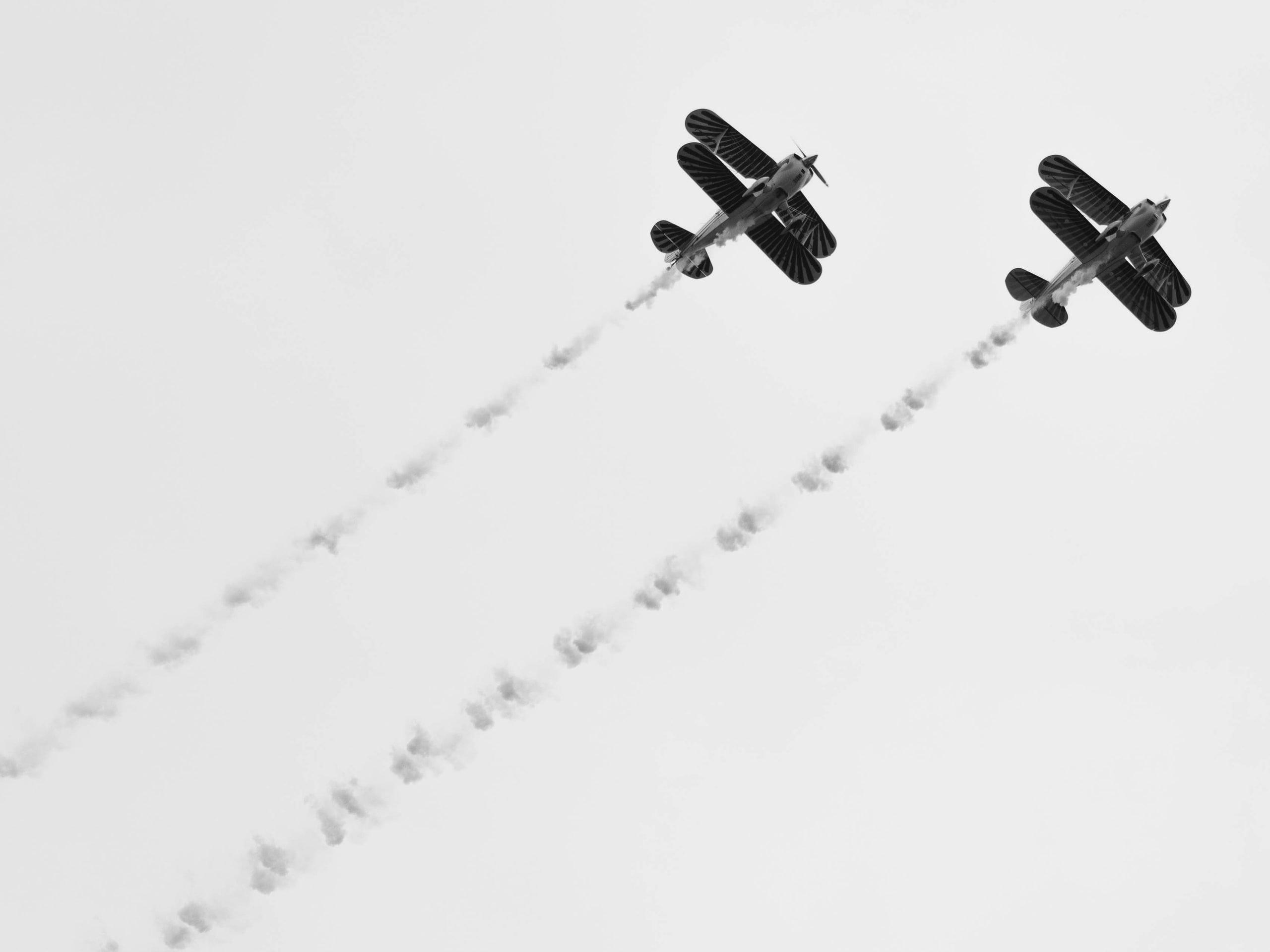 Two biplanes against white sky, the negative-space frame.