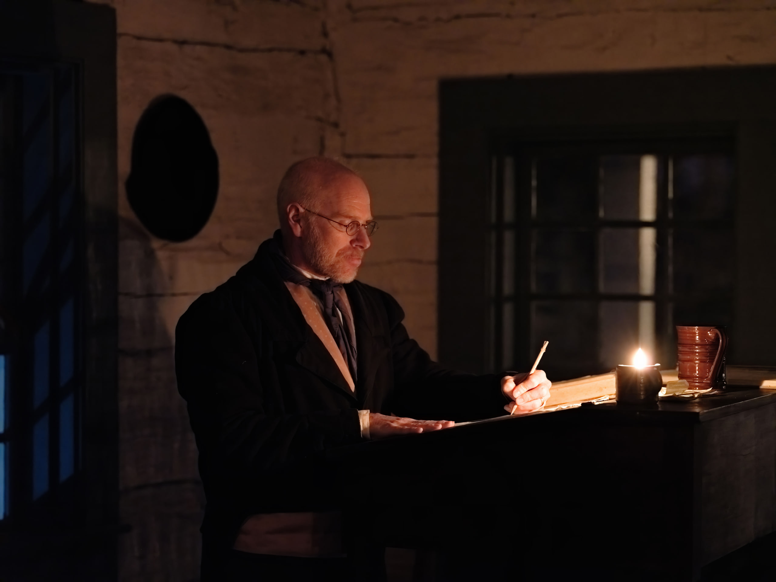Man at a desk by candlelight, one source.