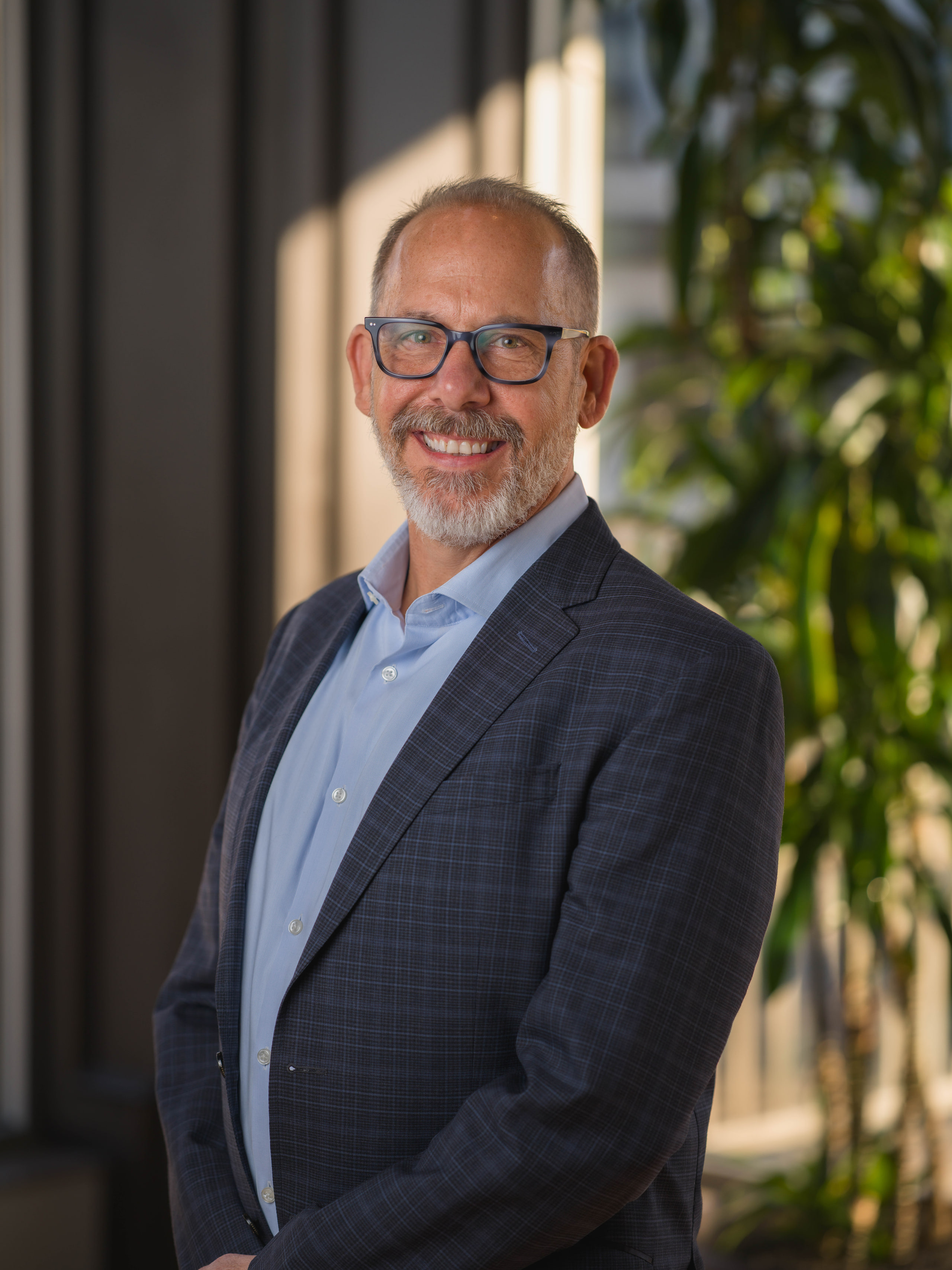 An environmental portrait: a man in a blue blazer against green foliage and window light